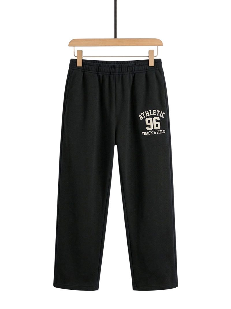 Black athletic sweatpants hanging on a wooden hanger against a white background, featuring a cream-colored 'ATHLETIC 96 TRACK & FIELD' graphic on the left thigh.